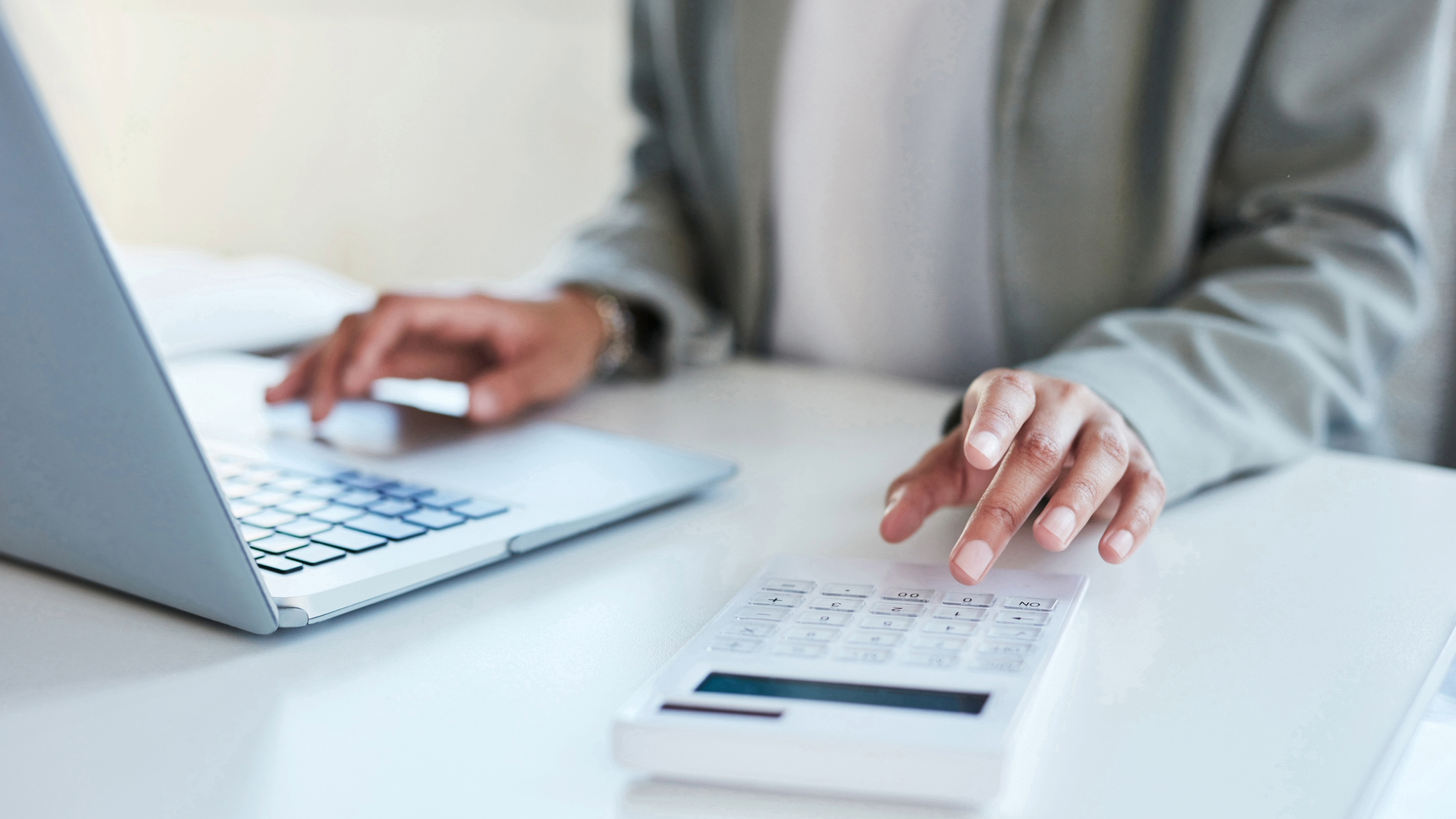 As mãos de uma pessoa usando uma calculadora e um laptop, para manter registros.