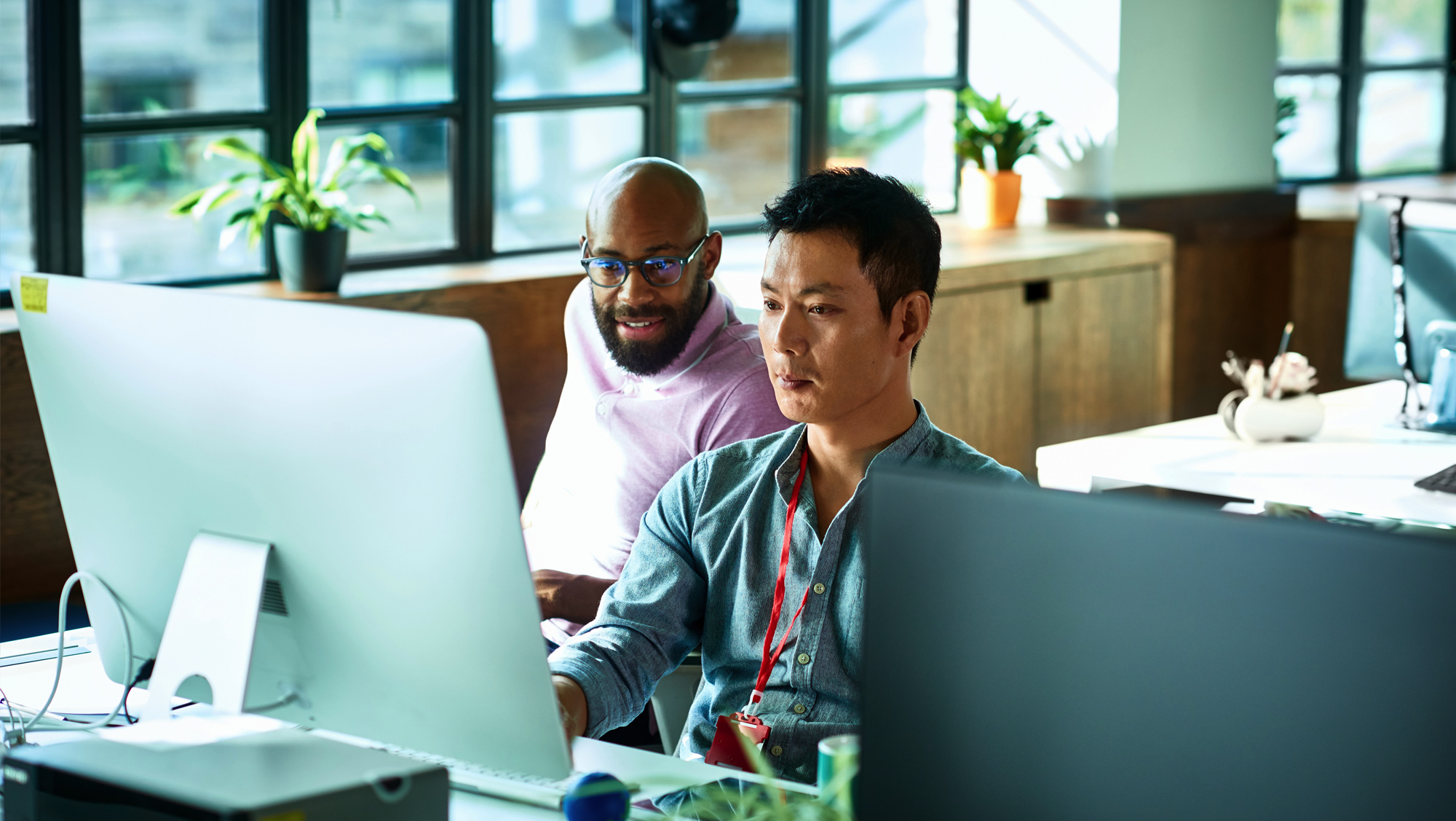 Dois colegas de trabalho examinam uma tela de computador em um escritório.