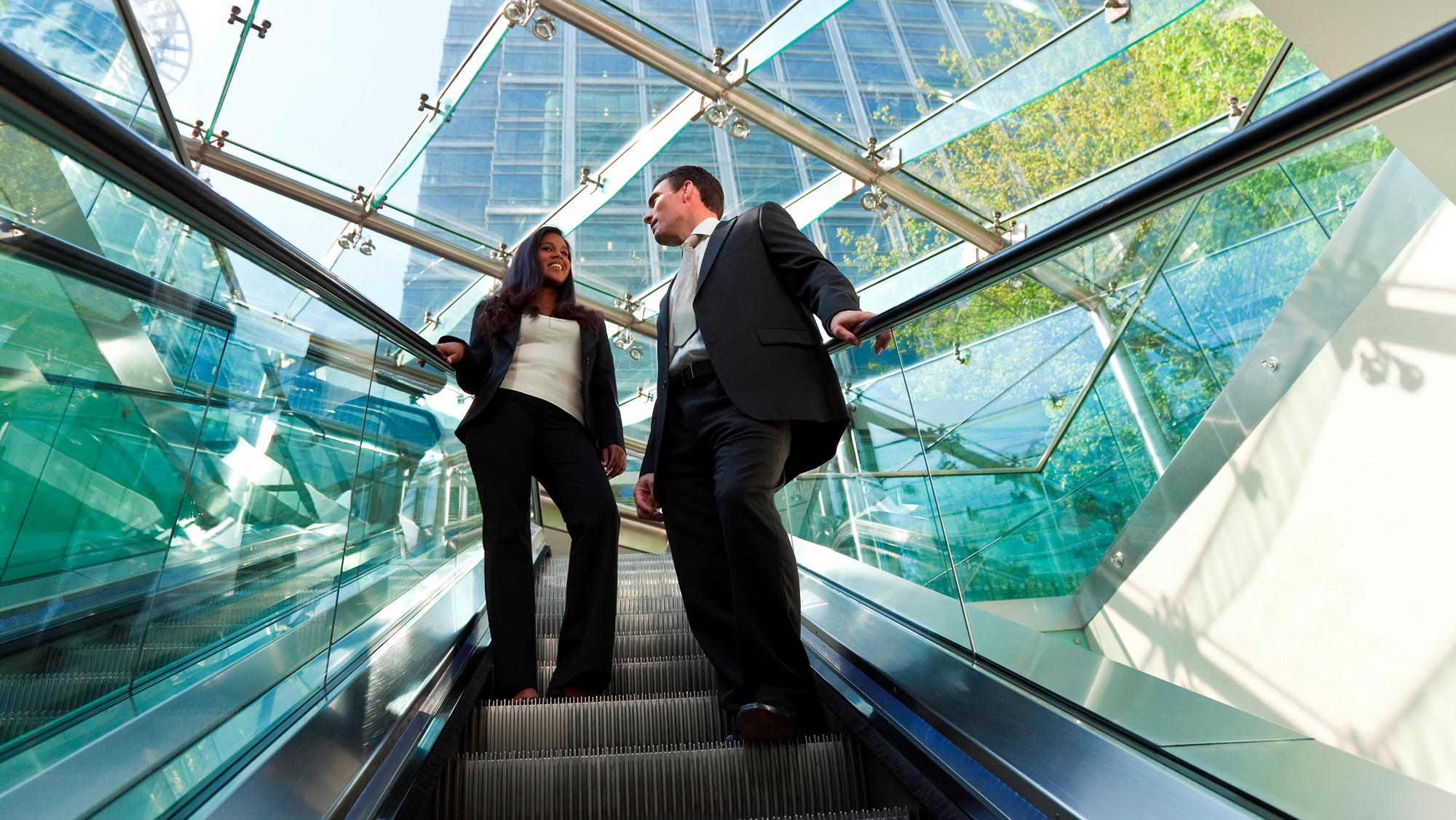 Dois colegas de trabalho andam na escada rolante em um prédio moderno.