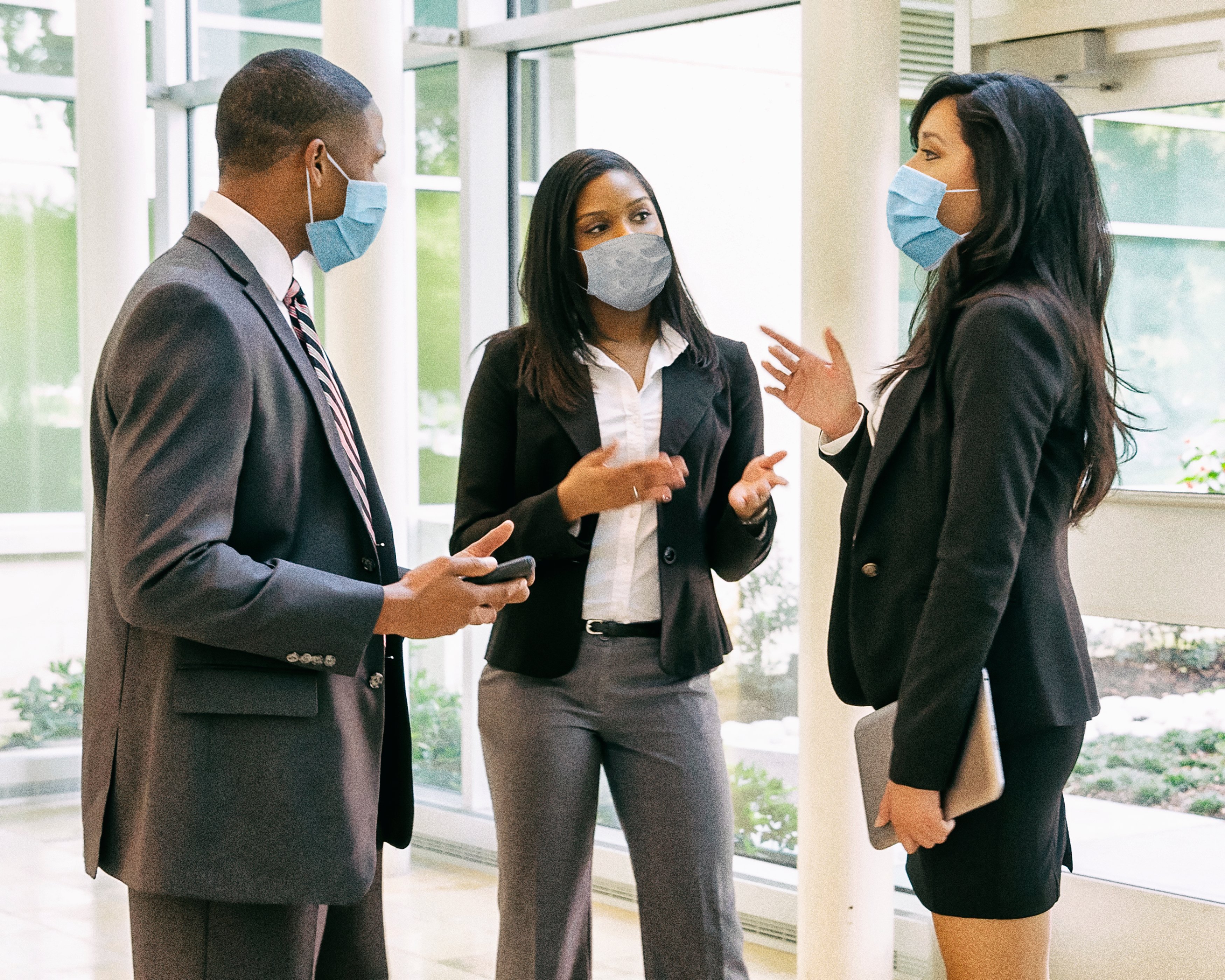 Três colegas de trabalho usando máscaras conversam em um escritório.
