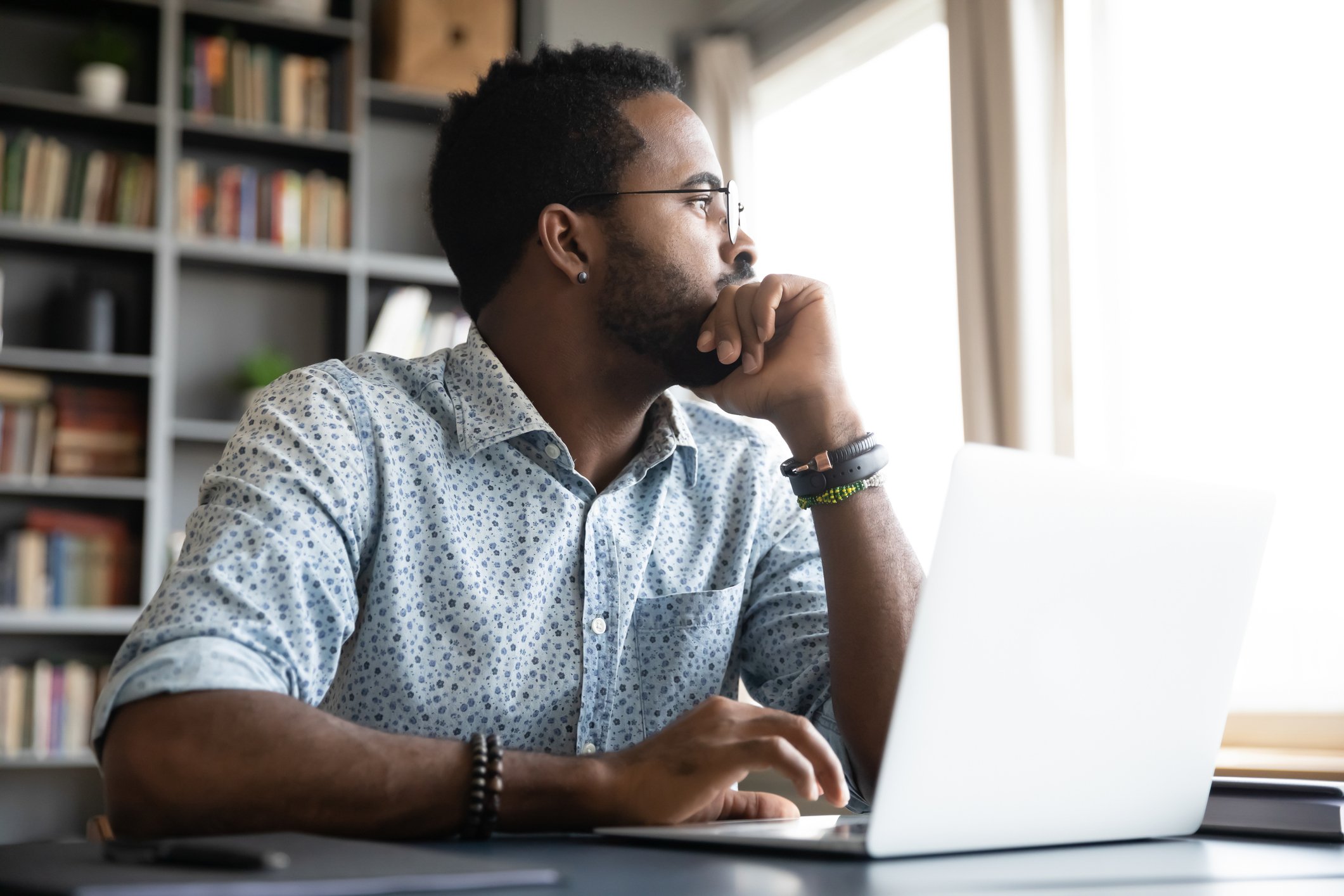Um homem contemplativo está sentado a uma mesa, usando um notebook.