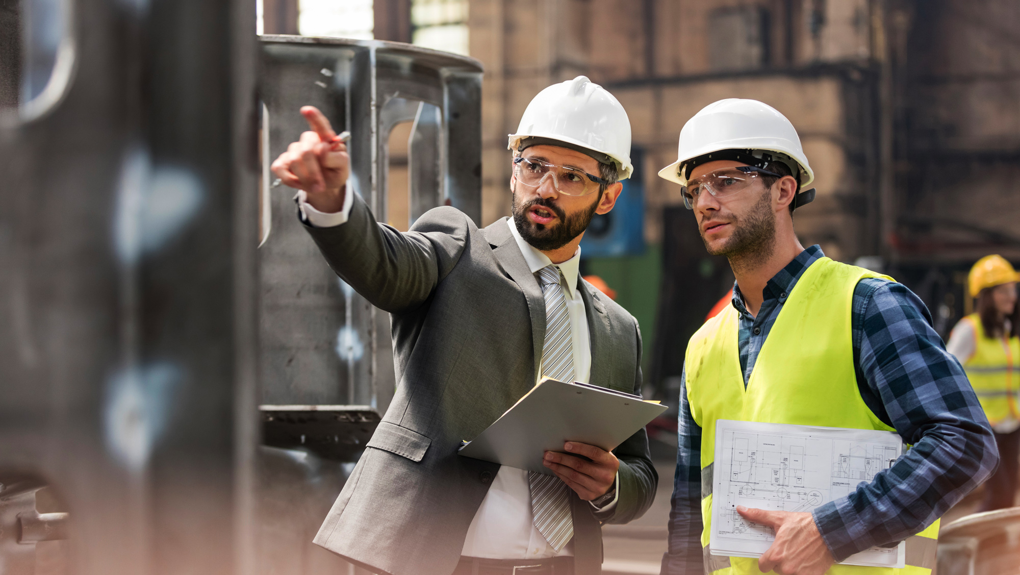 Duas pessoas no local, usando capacetes de segurança, discutindo um projeto.