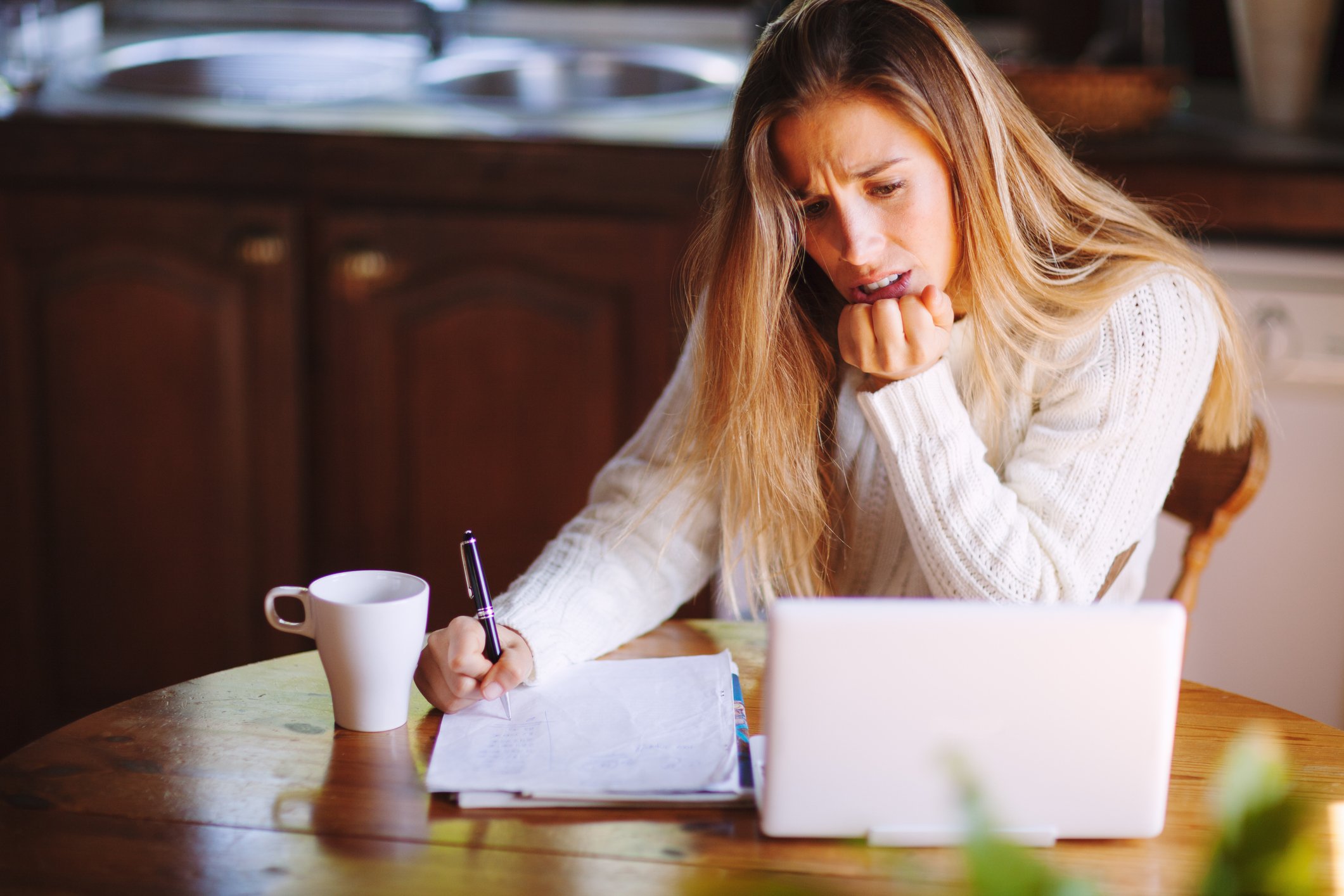 Mulher revisando documentos no notebook, com aparência estressada.