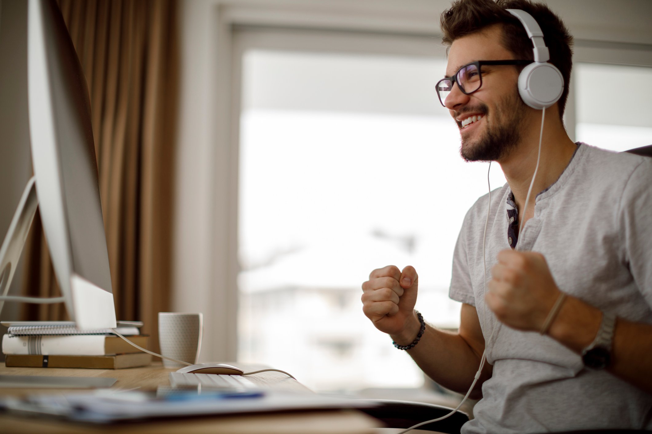 Homem sorridente com fones de ouvido comemora no computador.