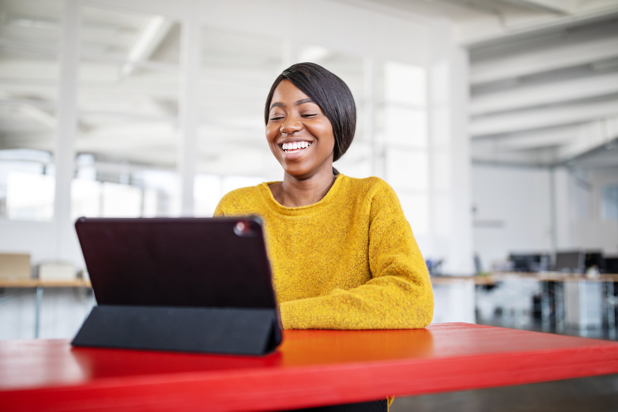 Mulher sorridente usando tablet na mesa.