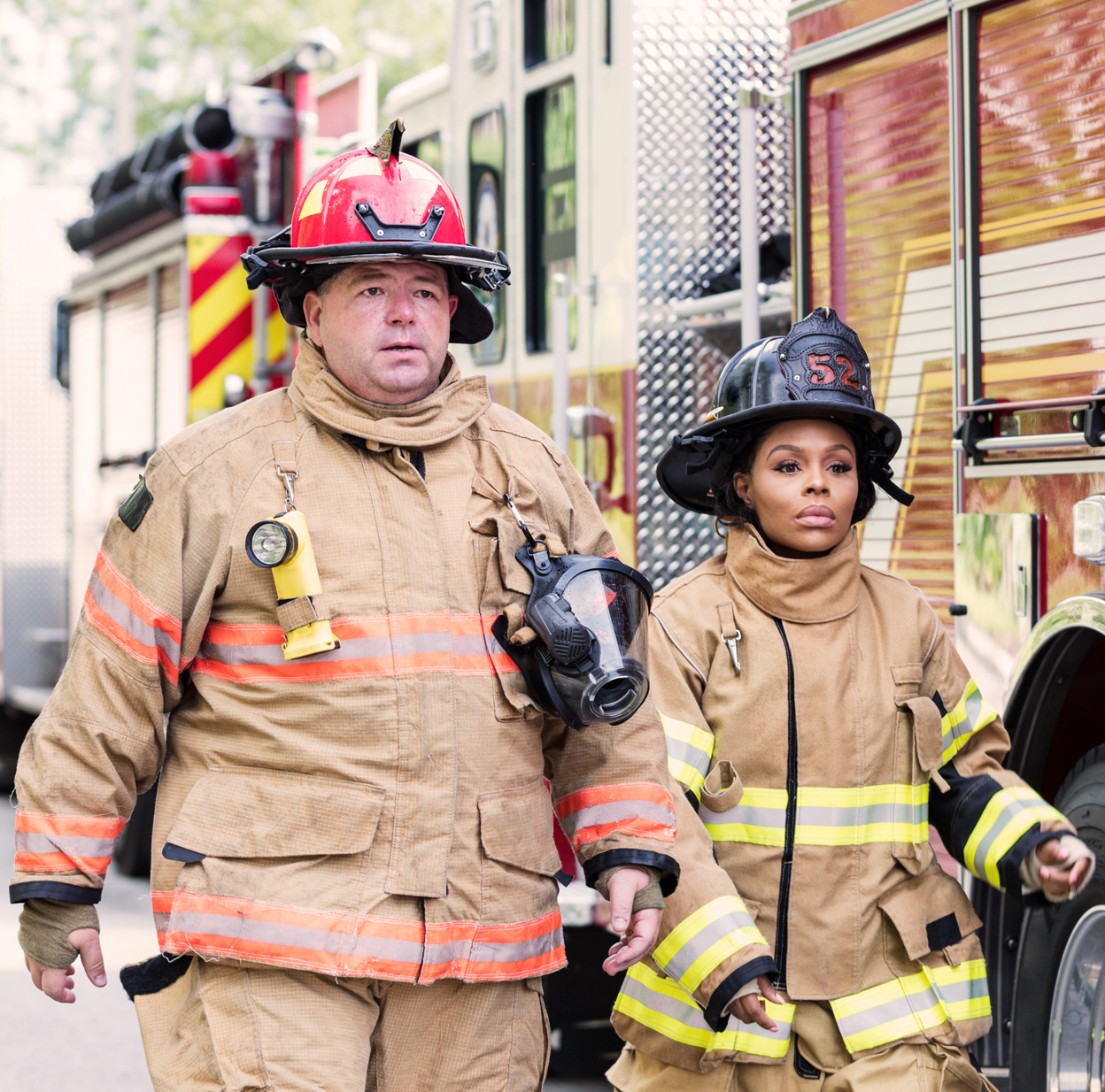 Two firefighters in protective gear are walking in front of a fire truck.