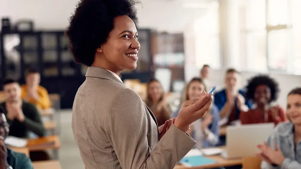 Smiling teacher addresses an applauding class.
