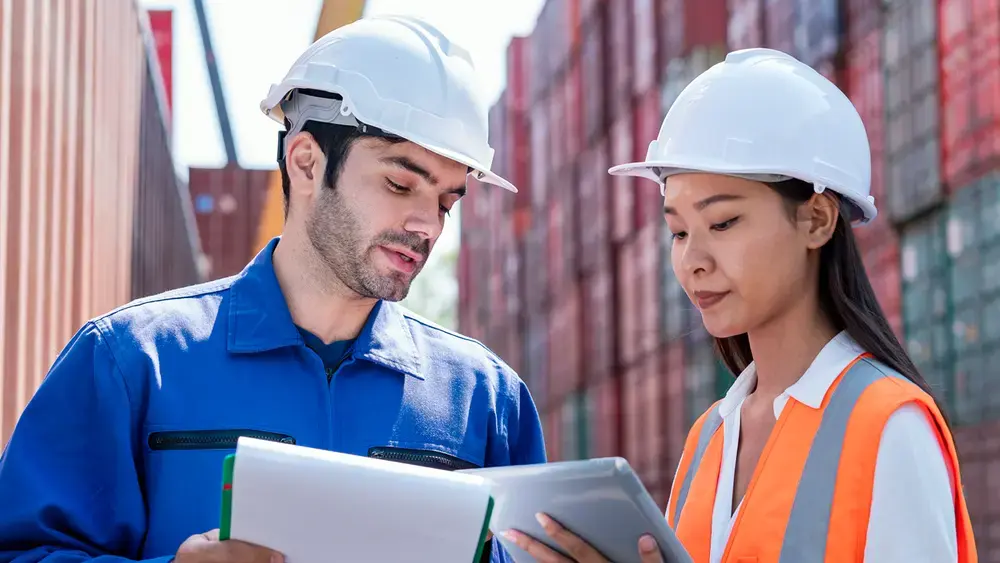 Coworkers review a datasheet at a container yard.