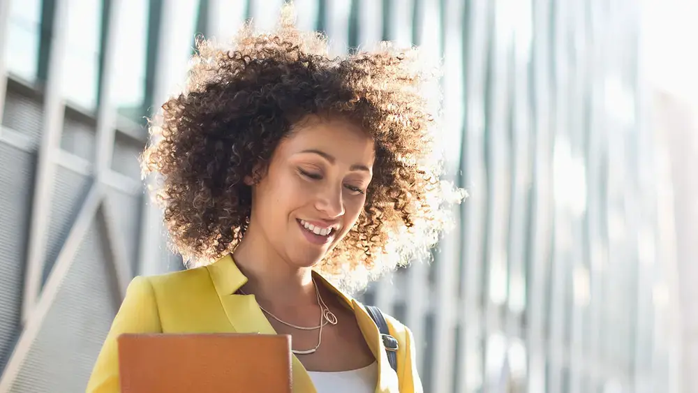 A woman in a yellow jacket smiles while using her smartphone.