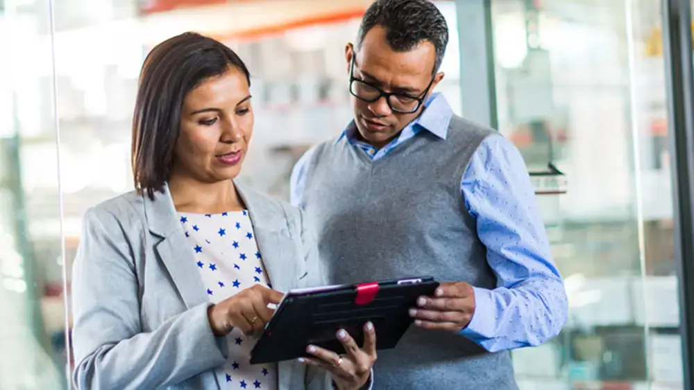 Dois colegas de trabalho olhando juntos para uma tela sensível ao toque.