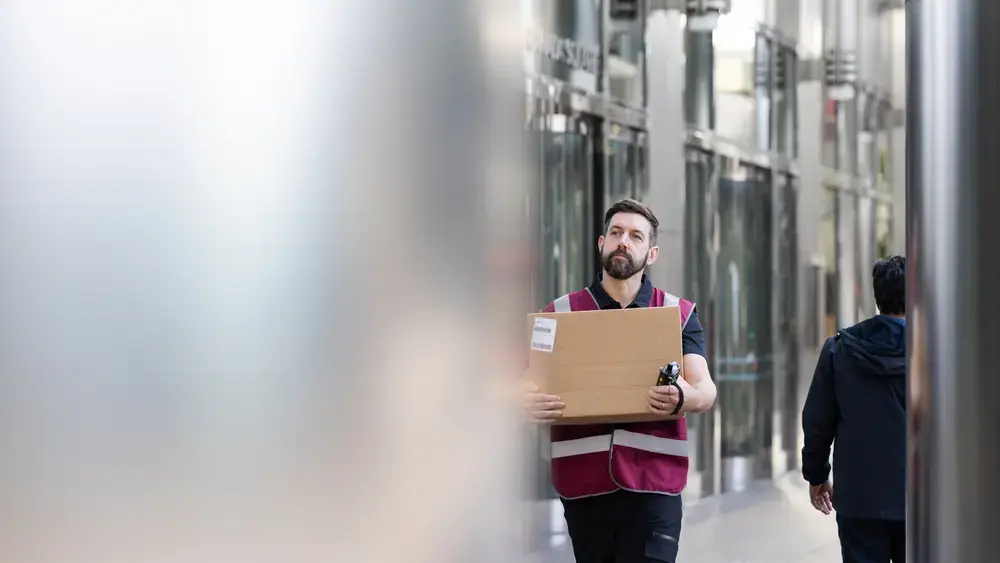 A man carries a box through a building hallway.