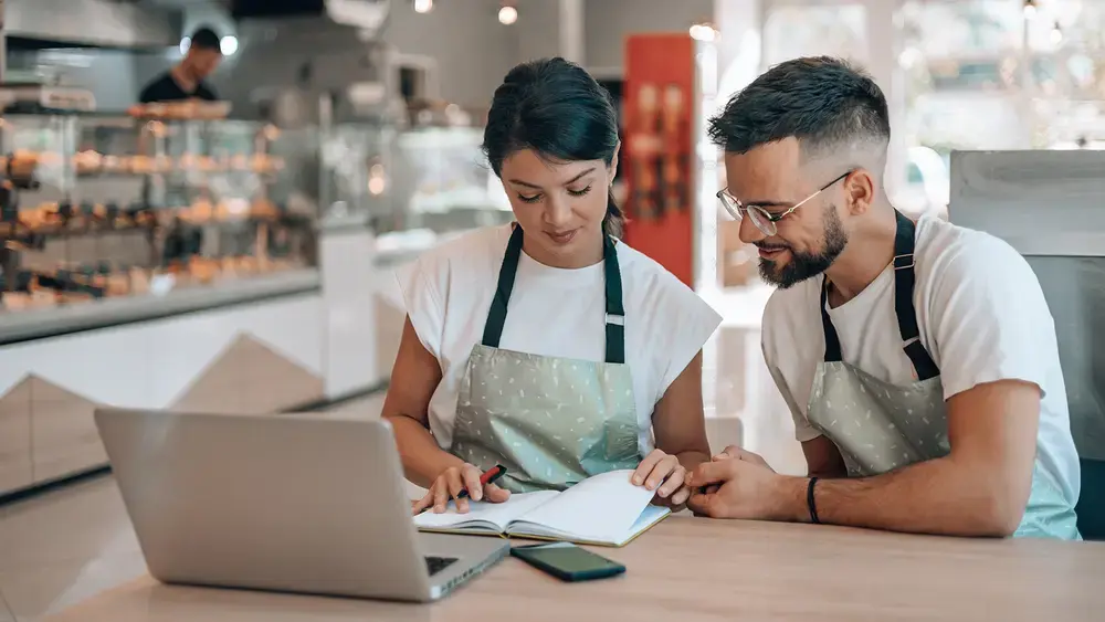 A coworker and a partner reviewing a timesheet at a cafe.