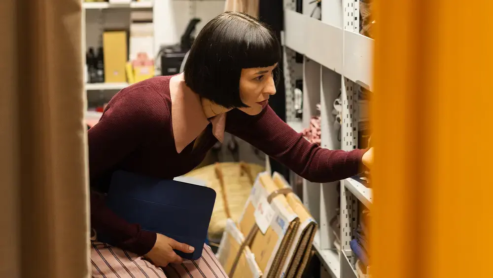 Coworker examines a shelf of materials, holding a blue notebook.