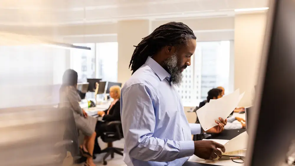 A man reviews paperwork in a busy office.