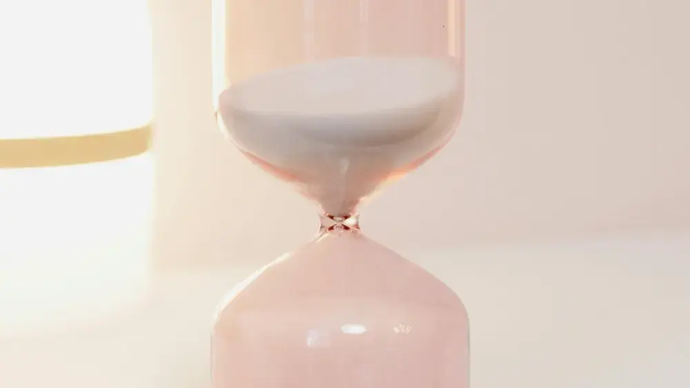Pink hourglass with sand slowly flowing.