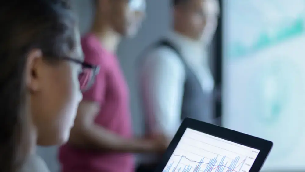 Woman uses a touchscreen to view a graph with coworkers in the background.