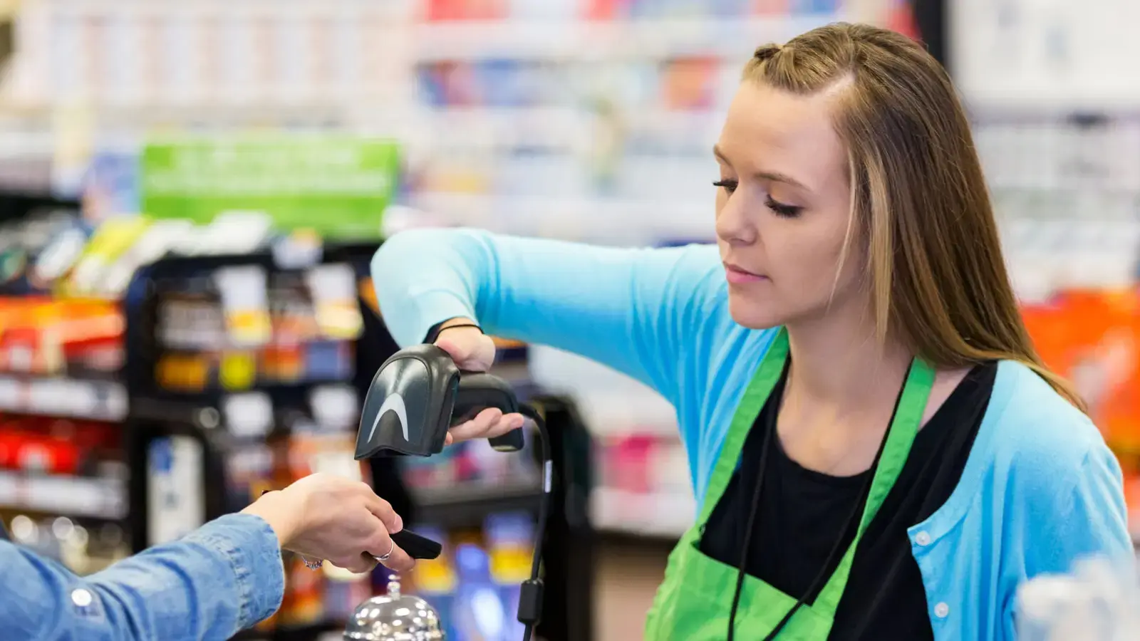 Woman cashier in green apron scans a customer's phone screen