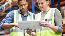 Two coworkers review a datasheet in a warehouse.