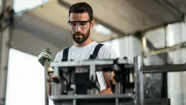 A focused worker in safety glasses operates machinery.