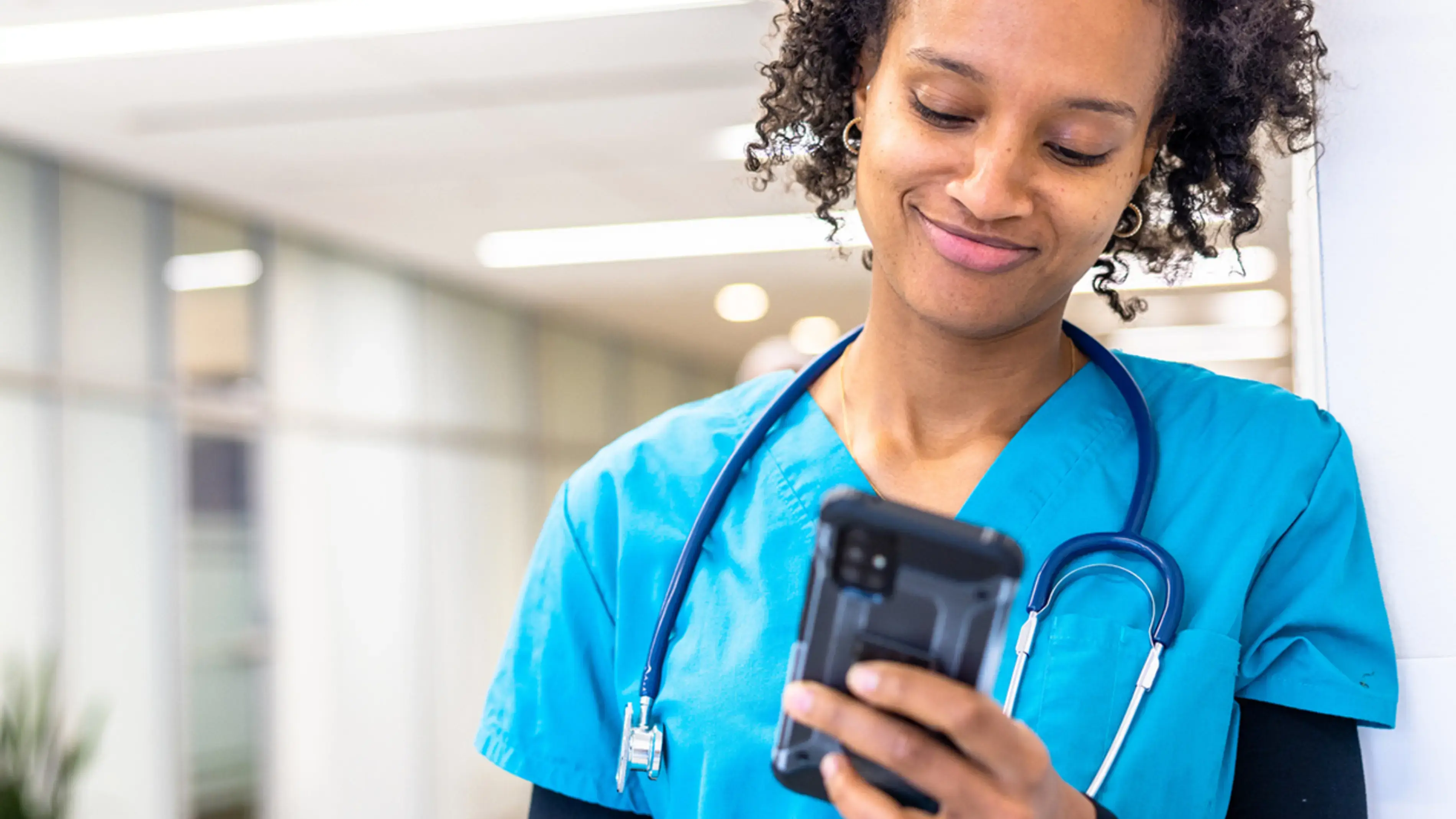 Nurse in blue scrubs looking at a smartphone, smiling.