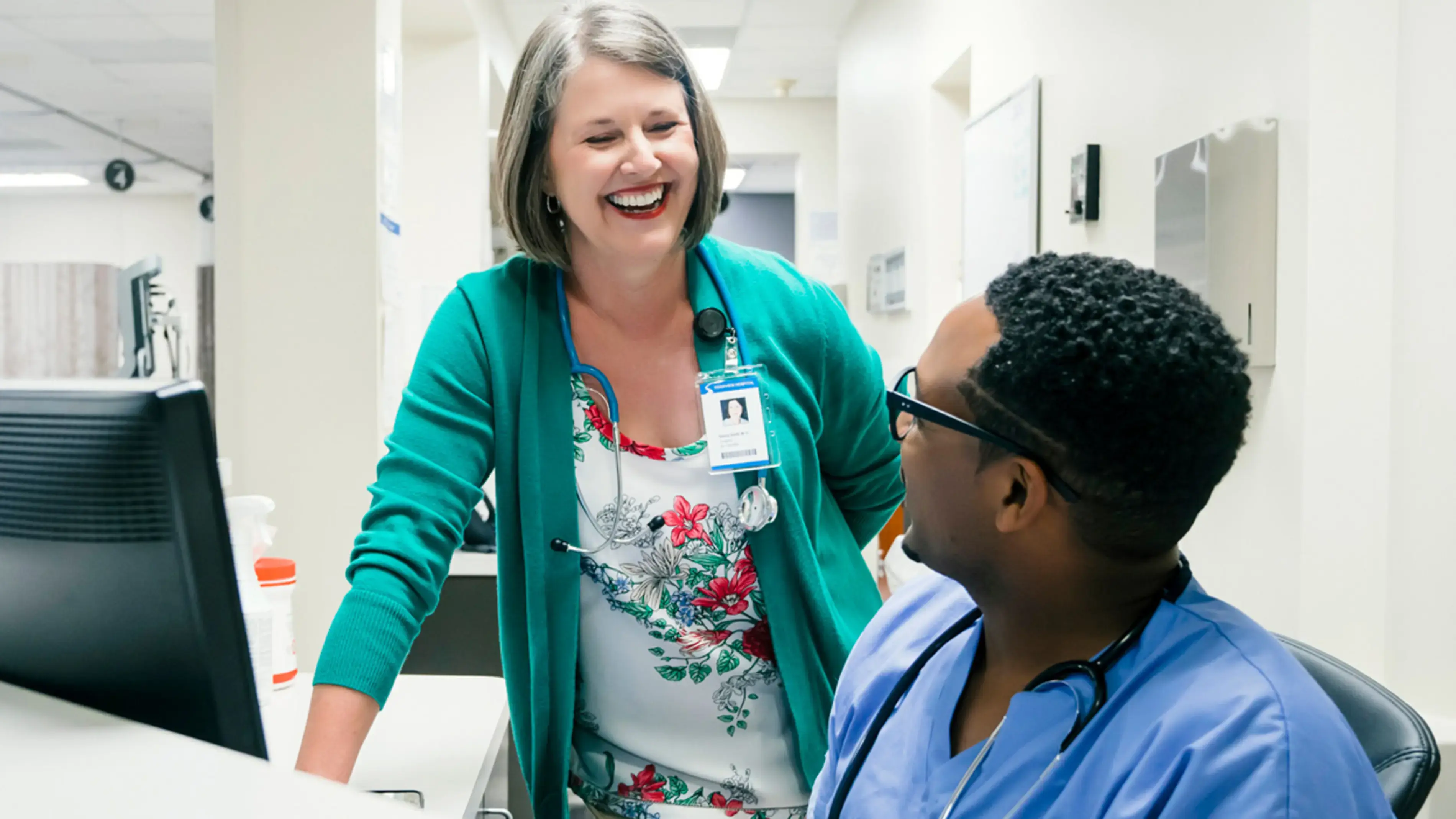 Two healthcare workers smiling at each other at a desk.
