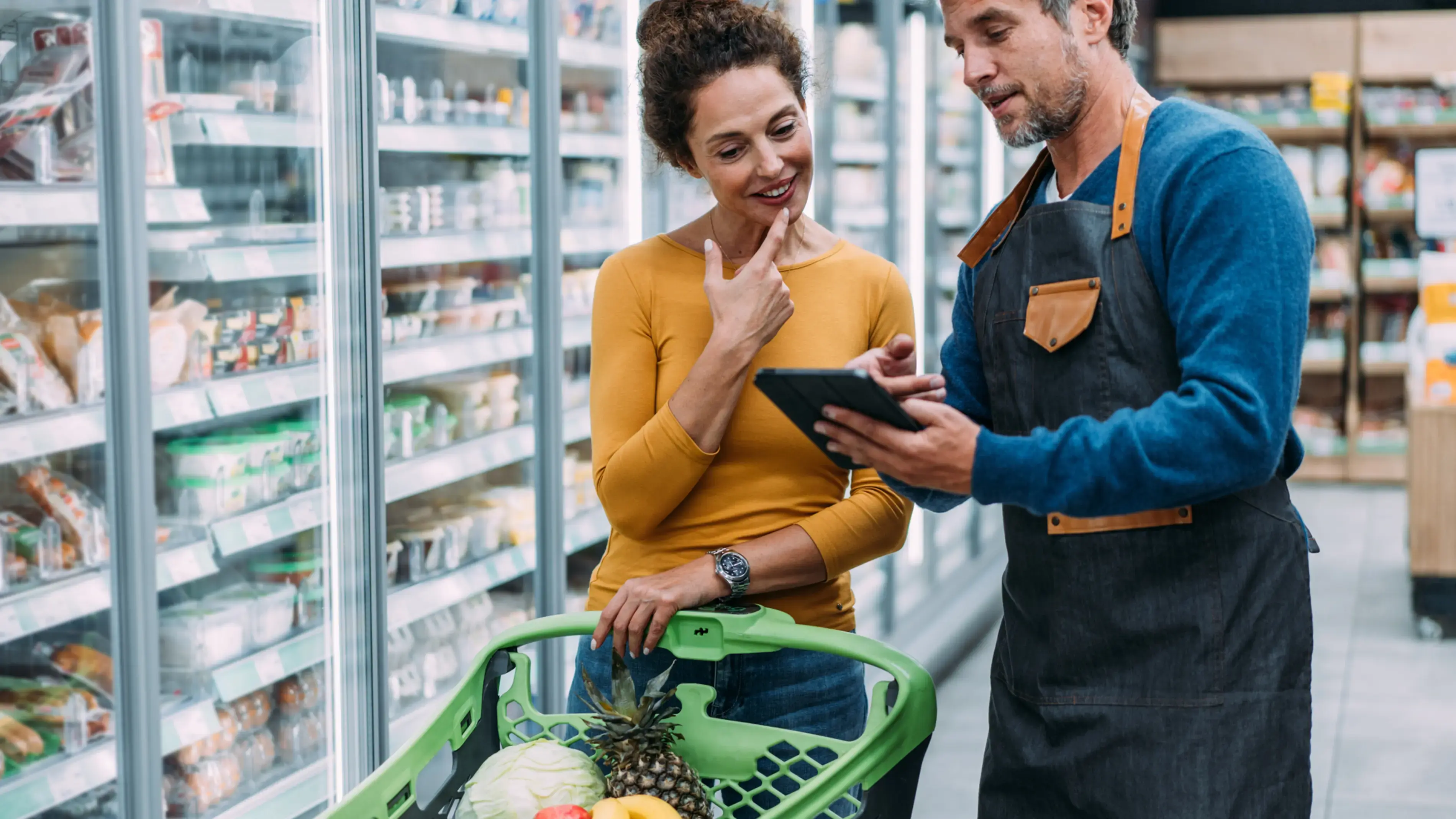 Funcionário de supermercado ajudando um cliente com um dispositivo de tela sensível ao toque.