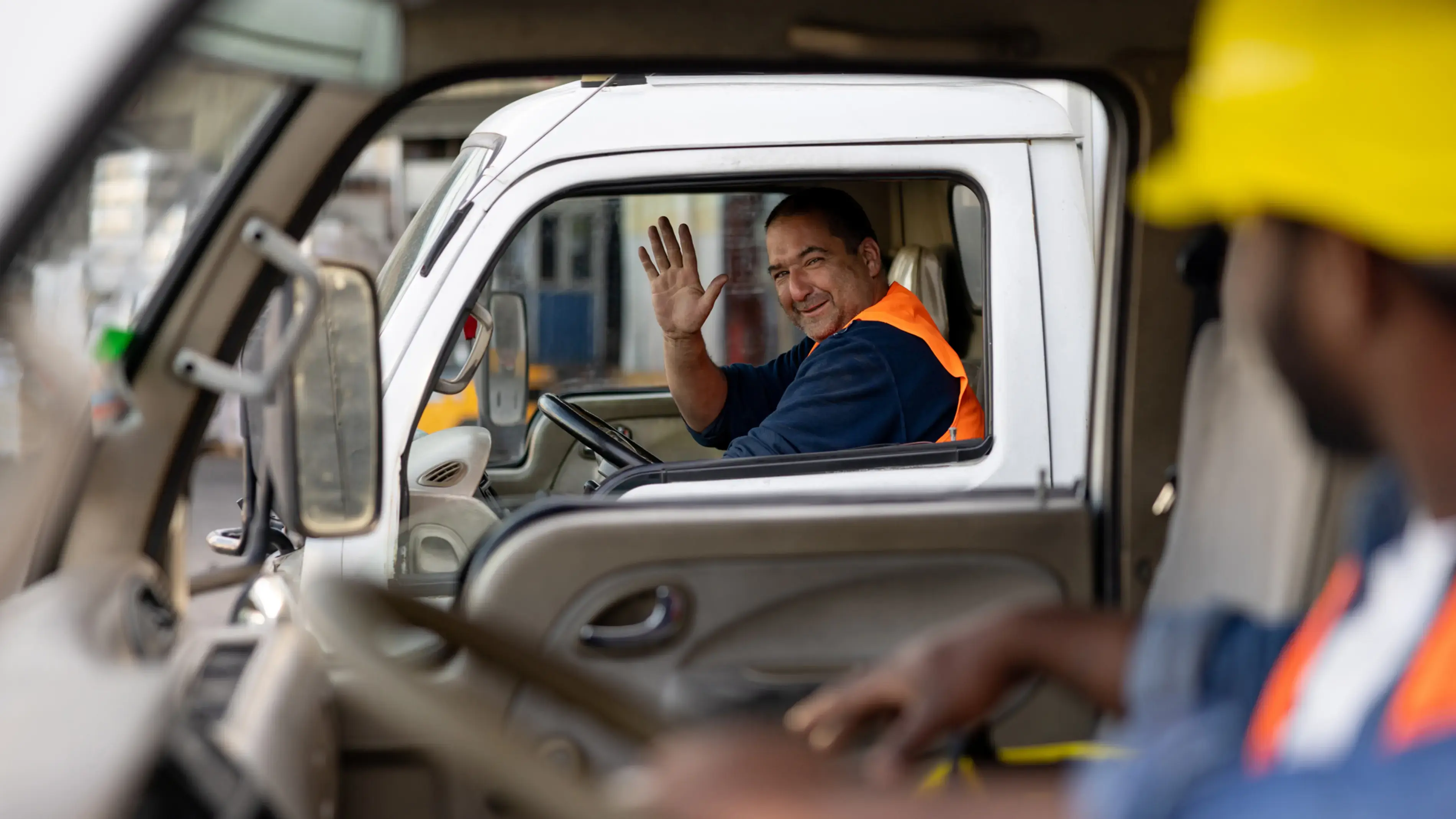 A driver waves from inside the truck to a coworker.