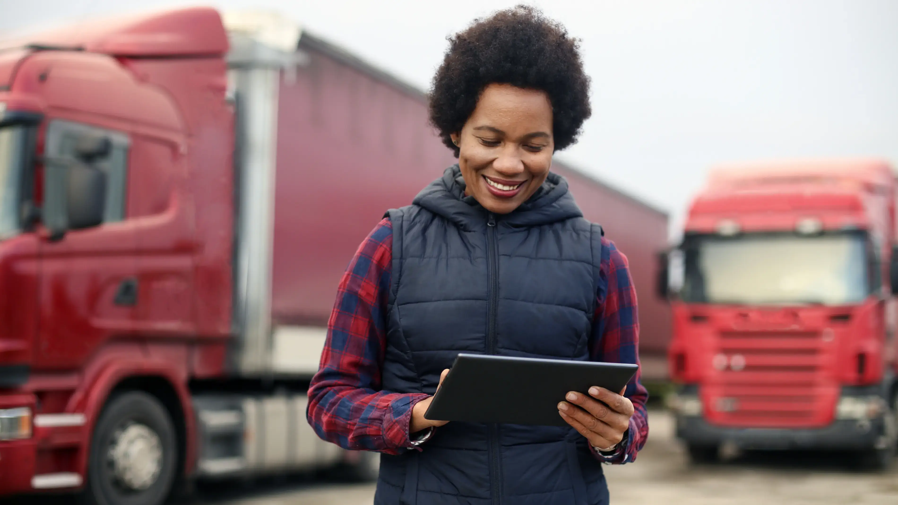 A woman with a smartphone stands in front of two red trucks.