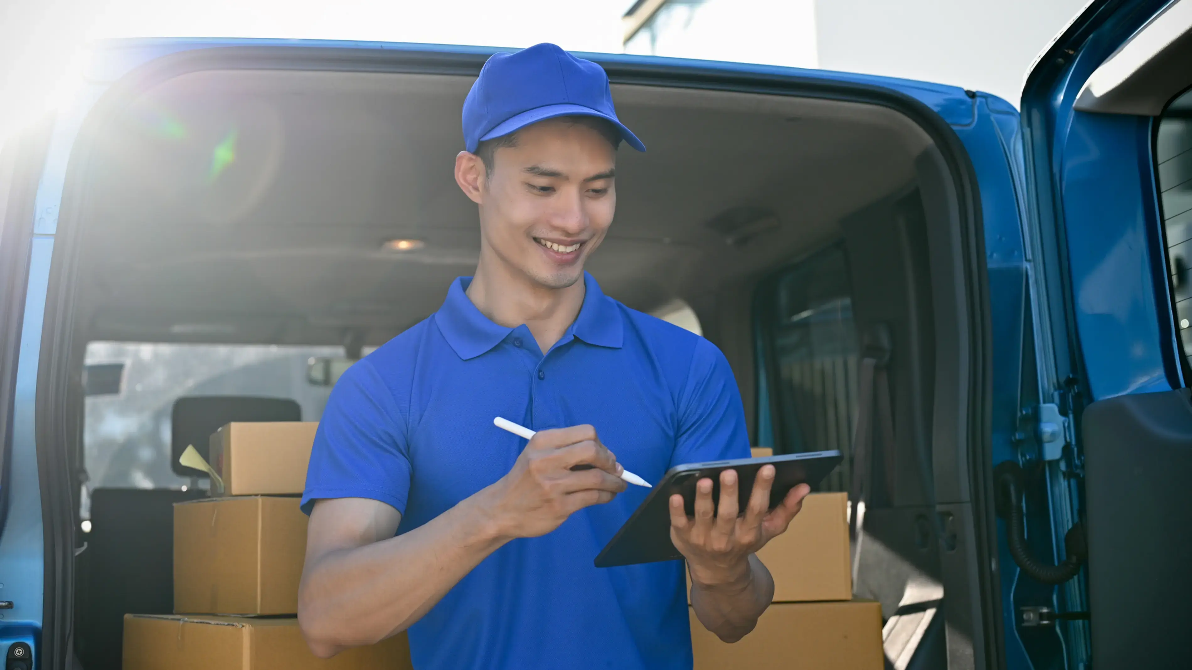 Delivery person using a touchscreen device with packages in a van.