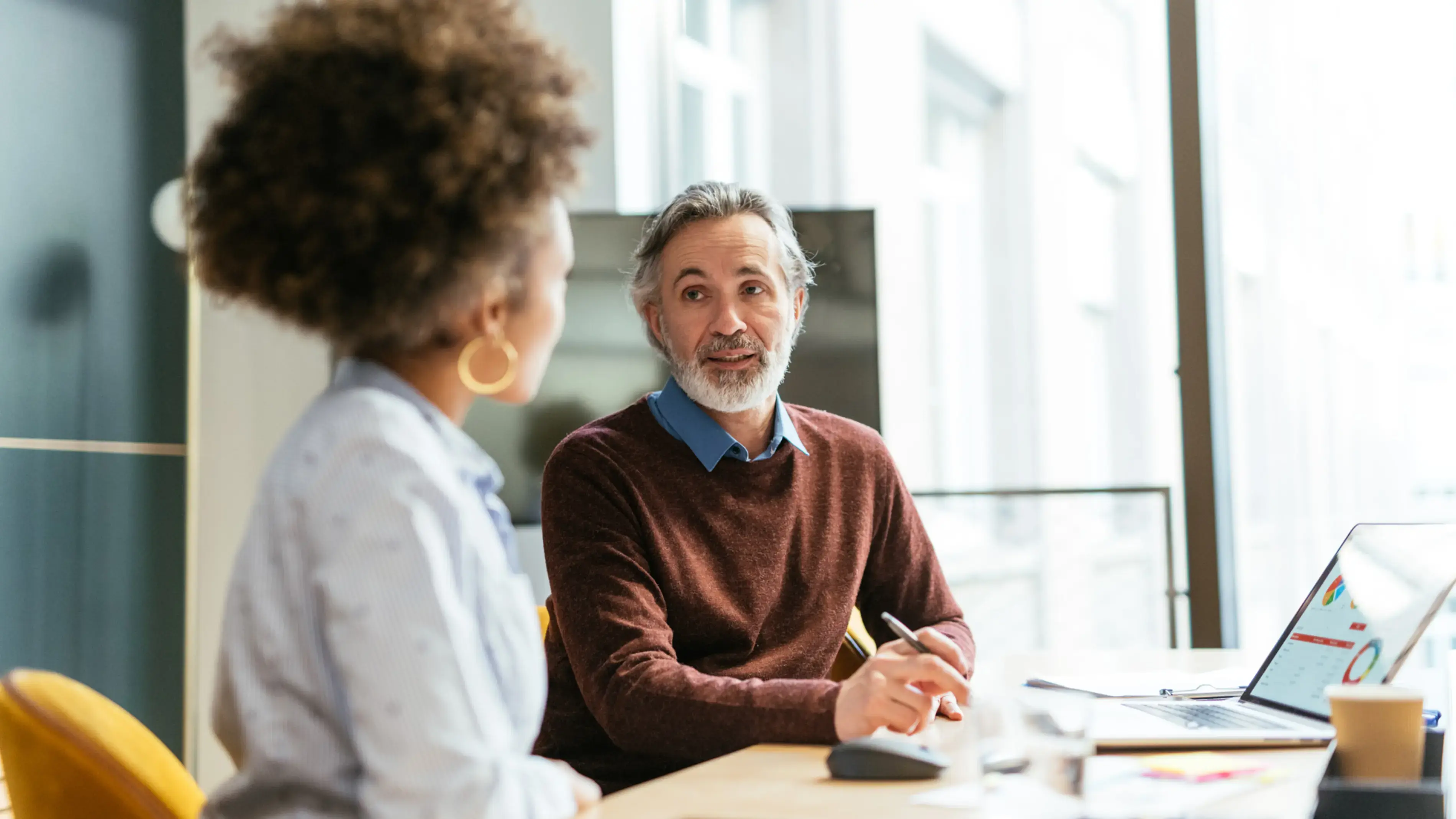 Two coworkers discuss a workflow displayed on a laptop.