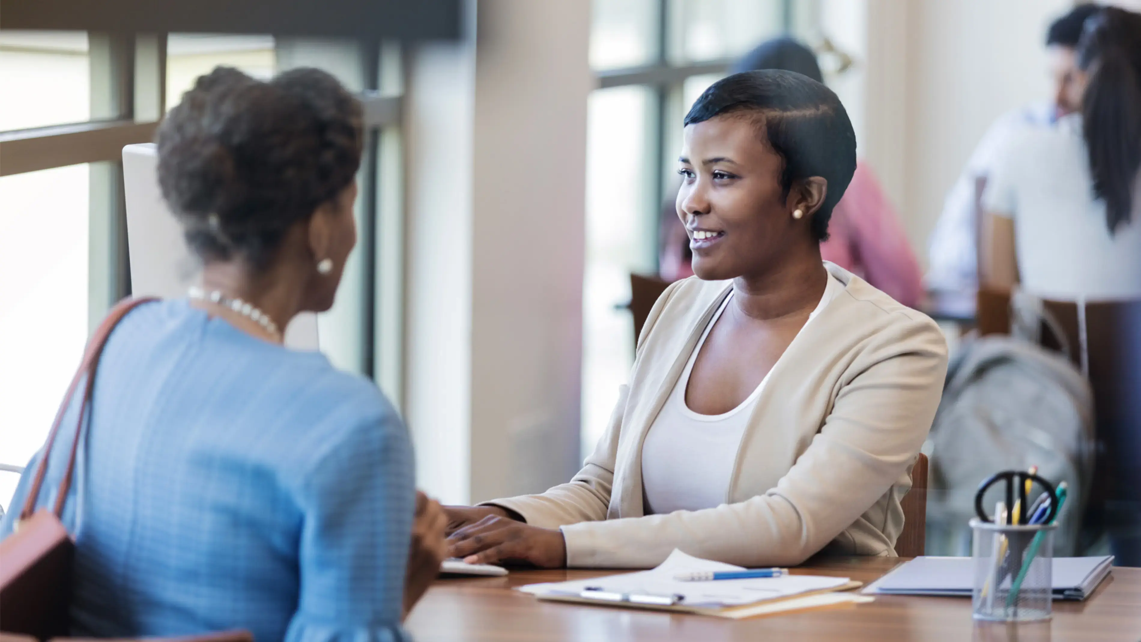 Two women in conversation at a roundtable, a workday environment.