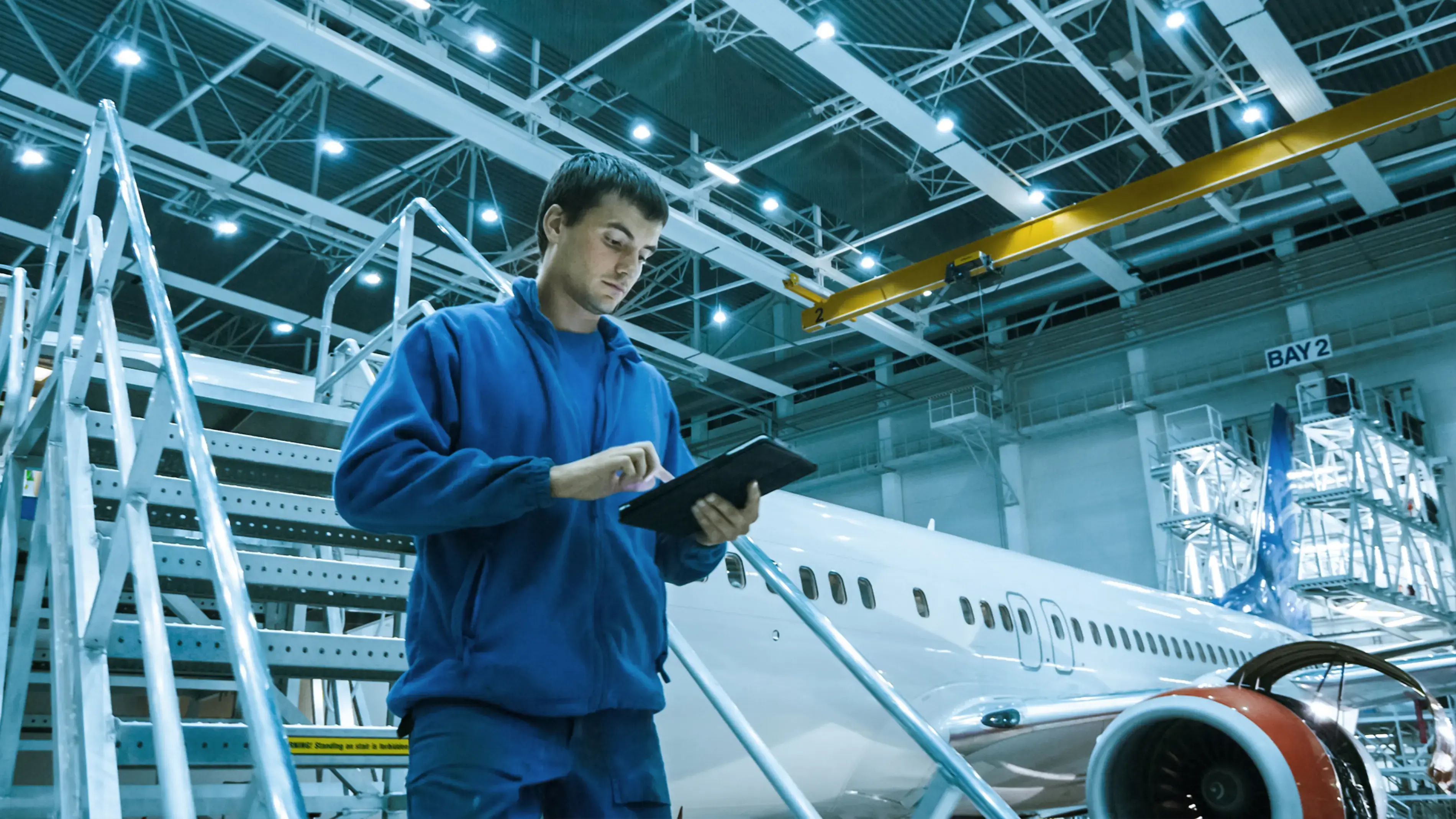 A man in a blue jumpsuit uses a touchscreen in a hangar.