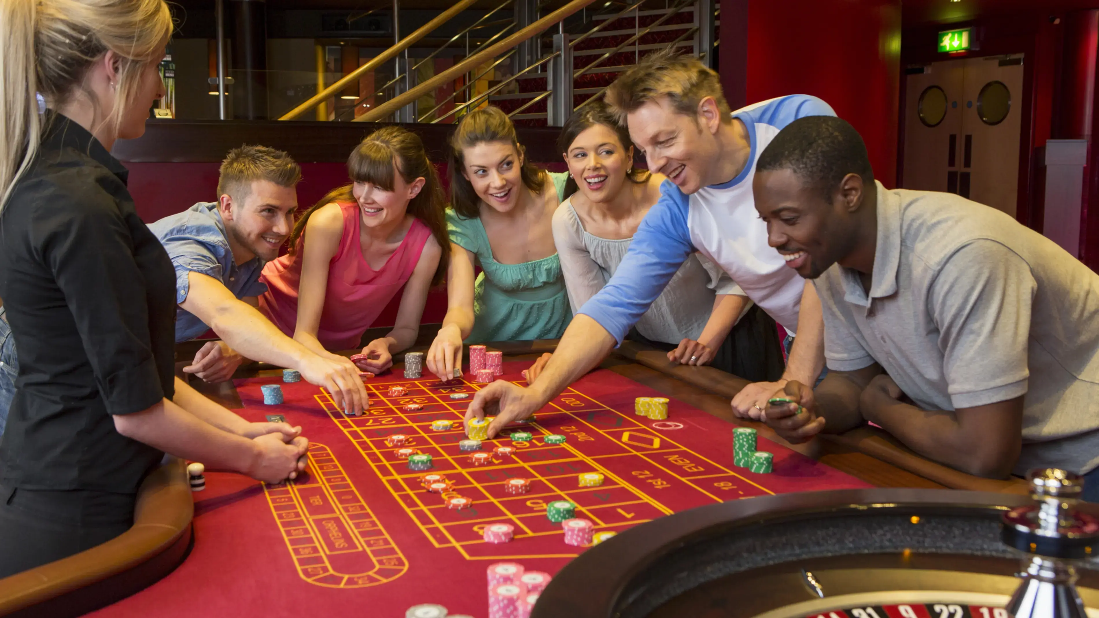 Casino table with people playing and the roulette wheel.