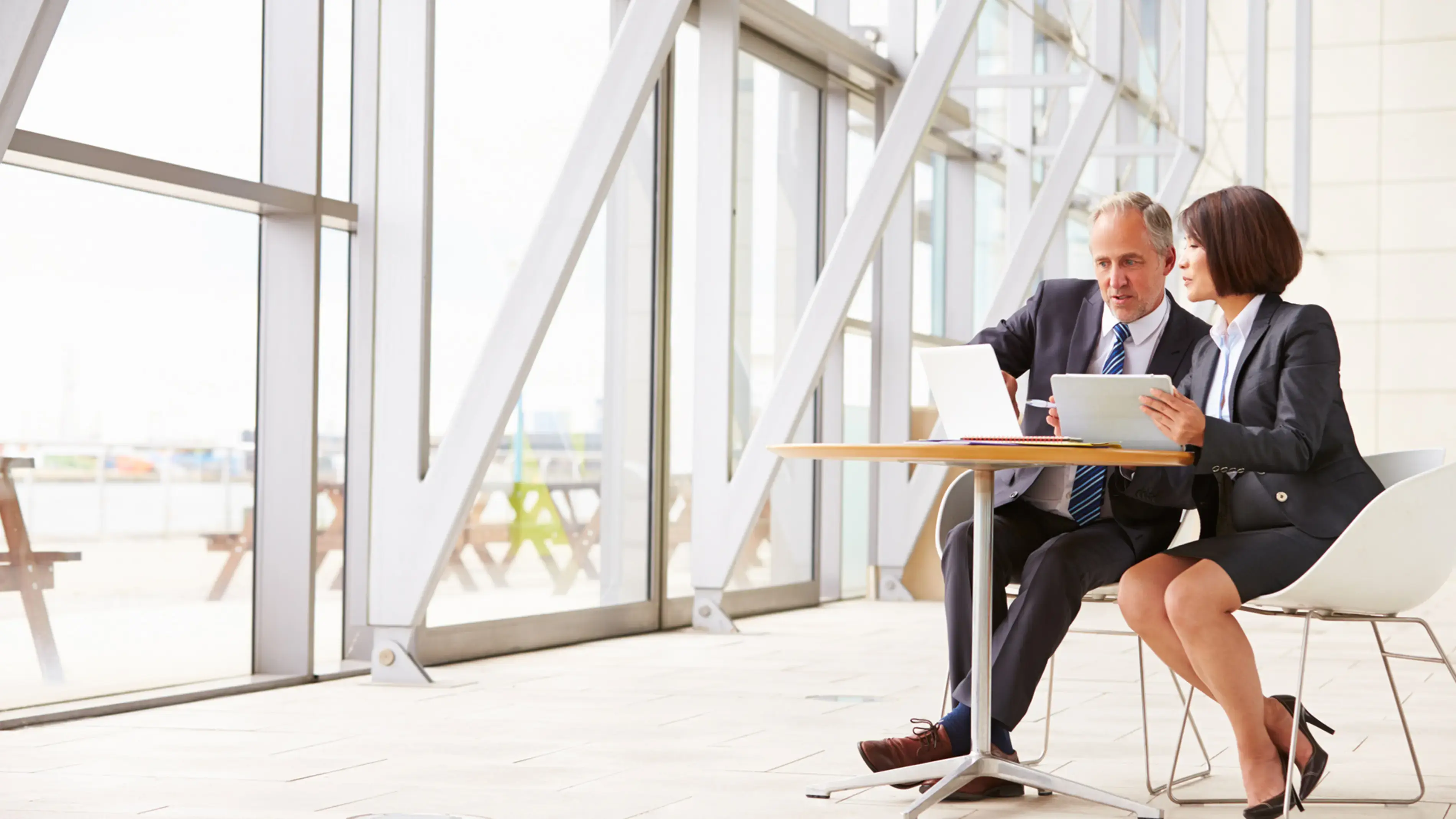 Dois colegas de trabalho de terno colaboram perto de uma janela.