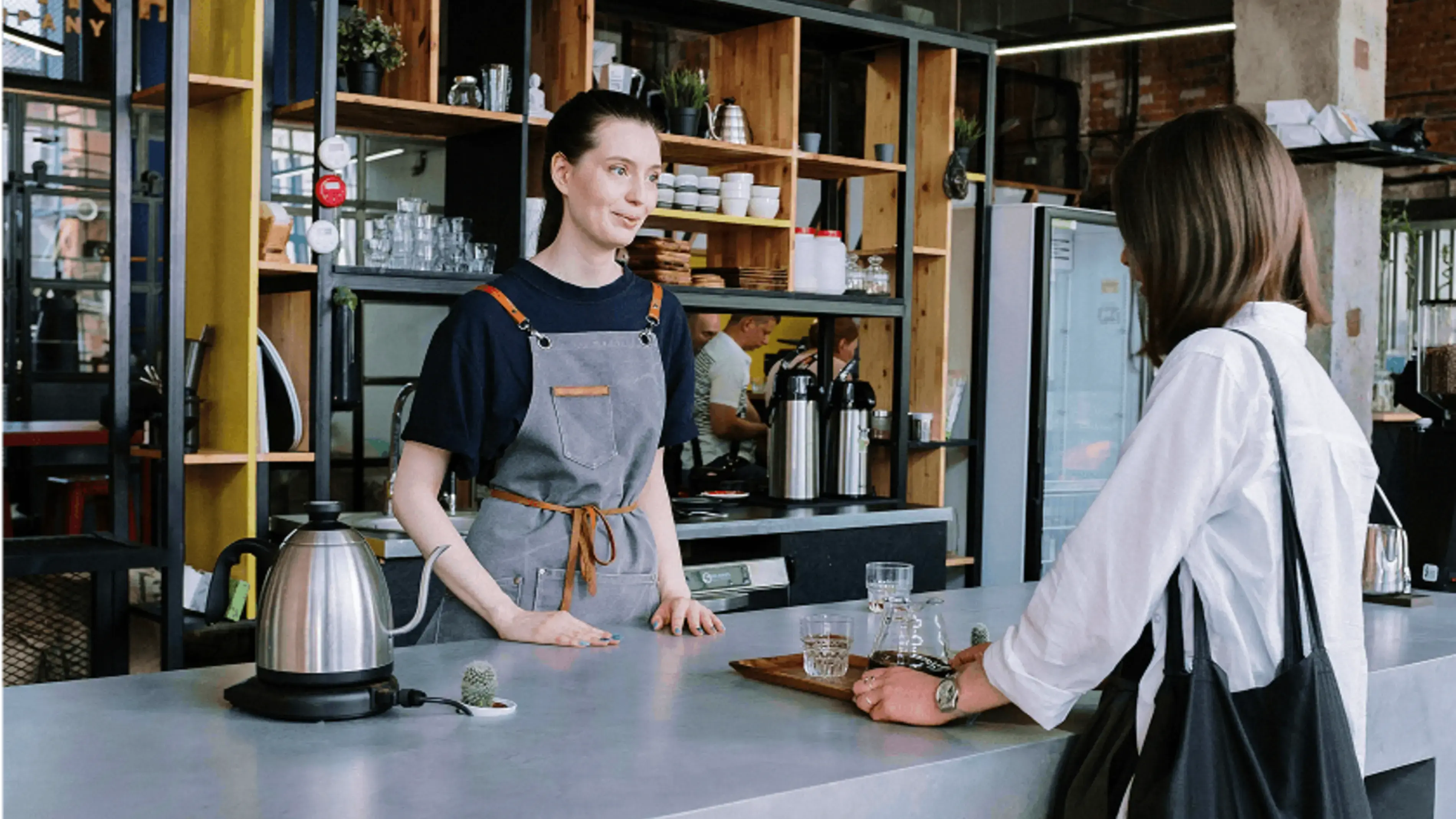 A barista helps a customer at a coffee shop counter.