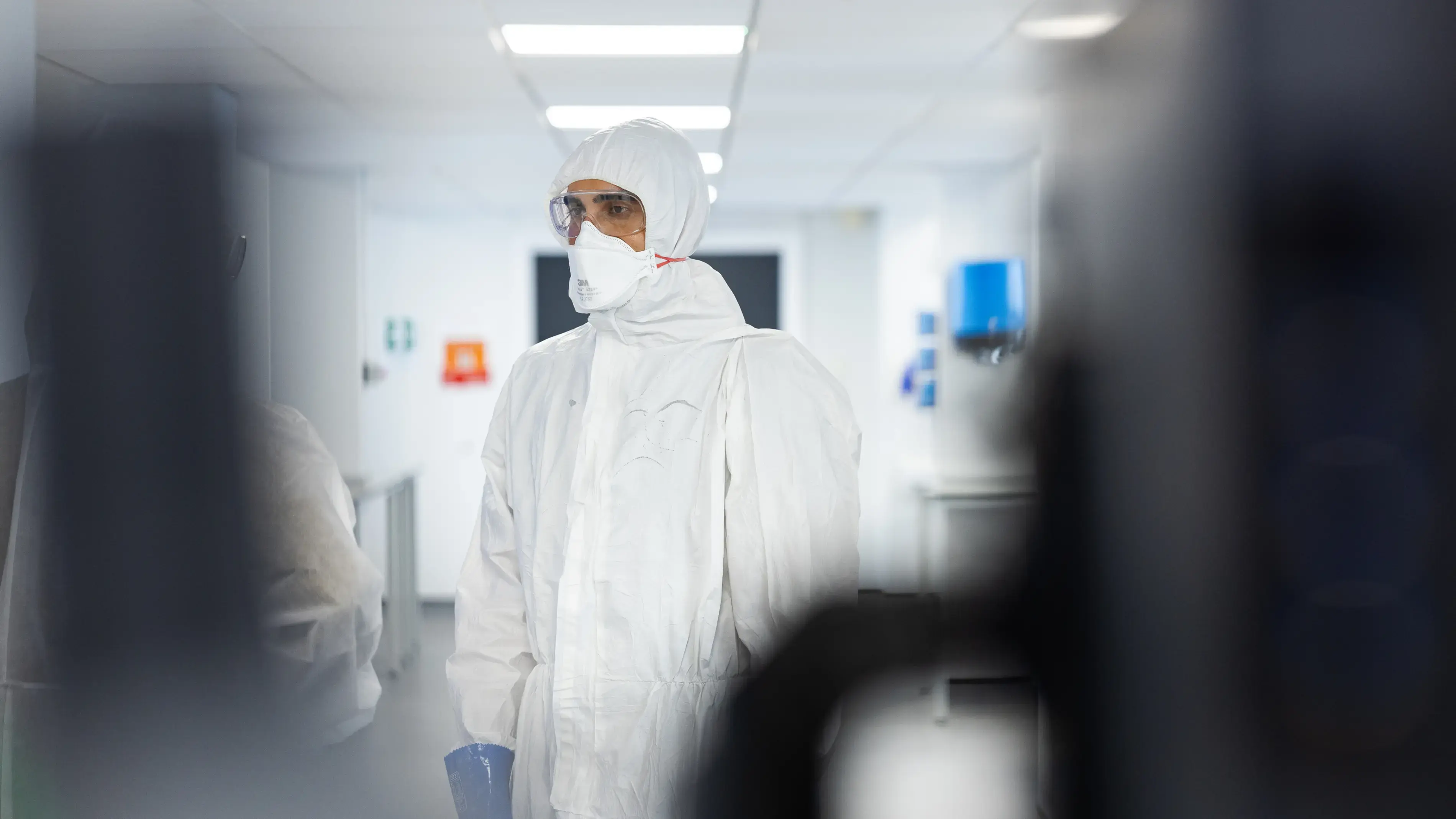 Person in a white protective suit walks down a hallway.