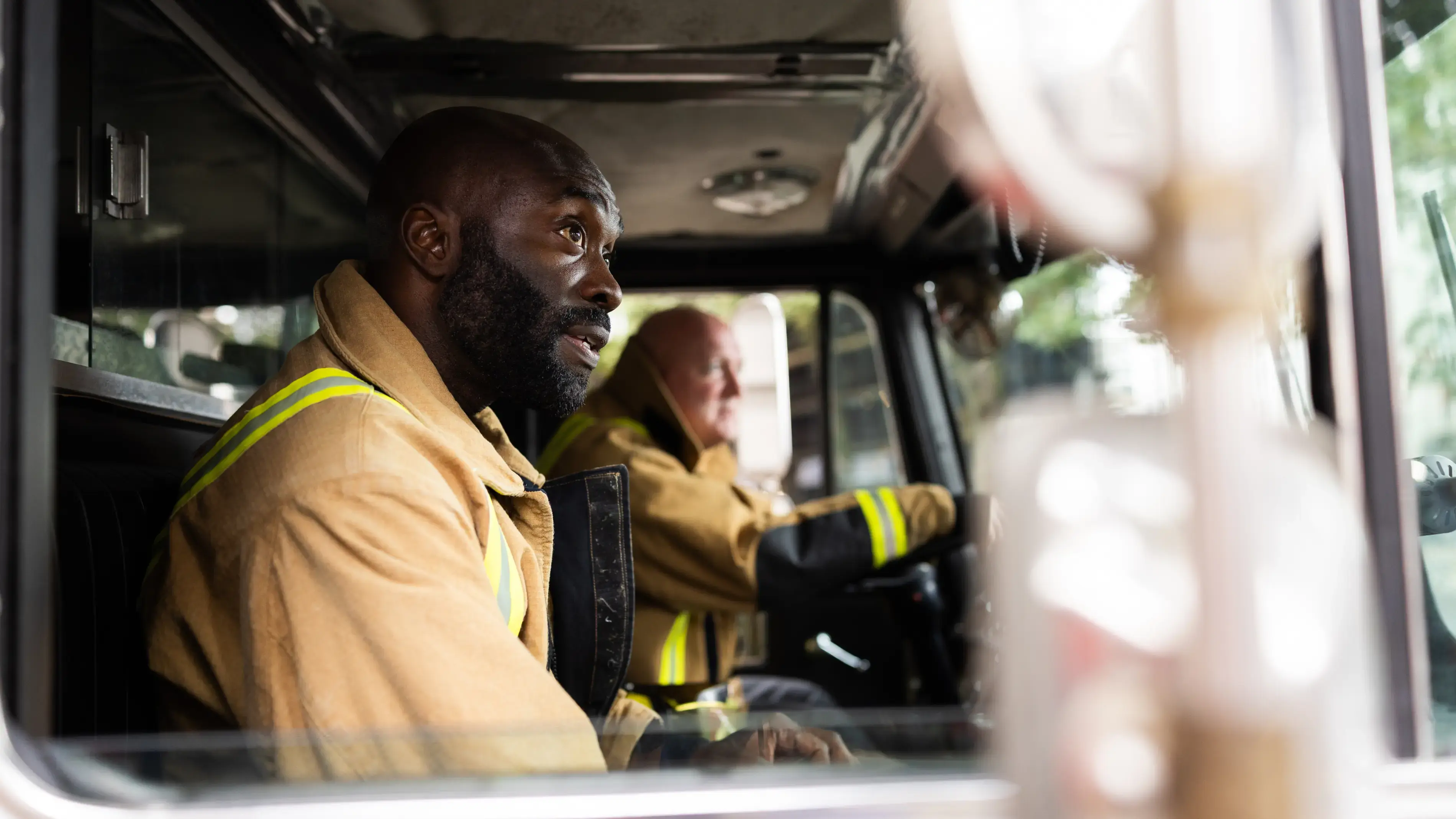 Two firefighters seated in a firetruck cab.