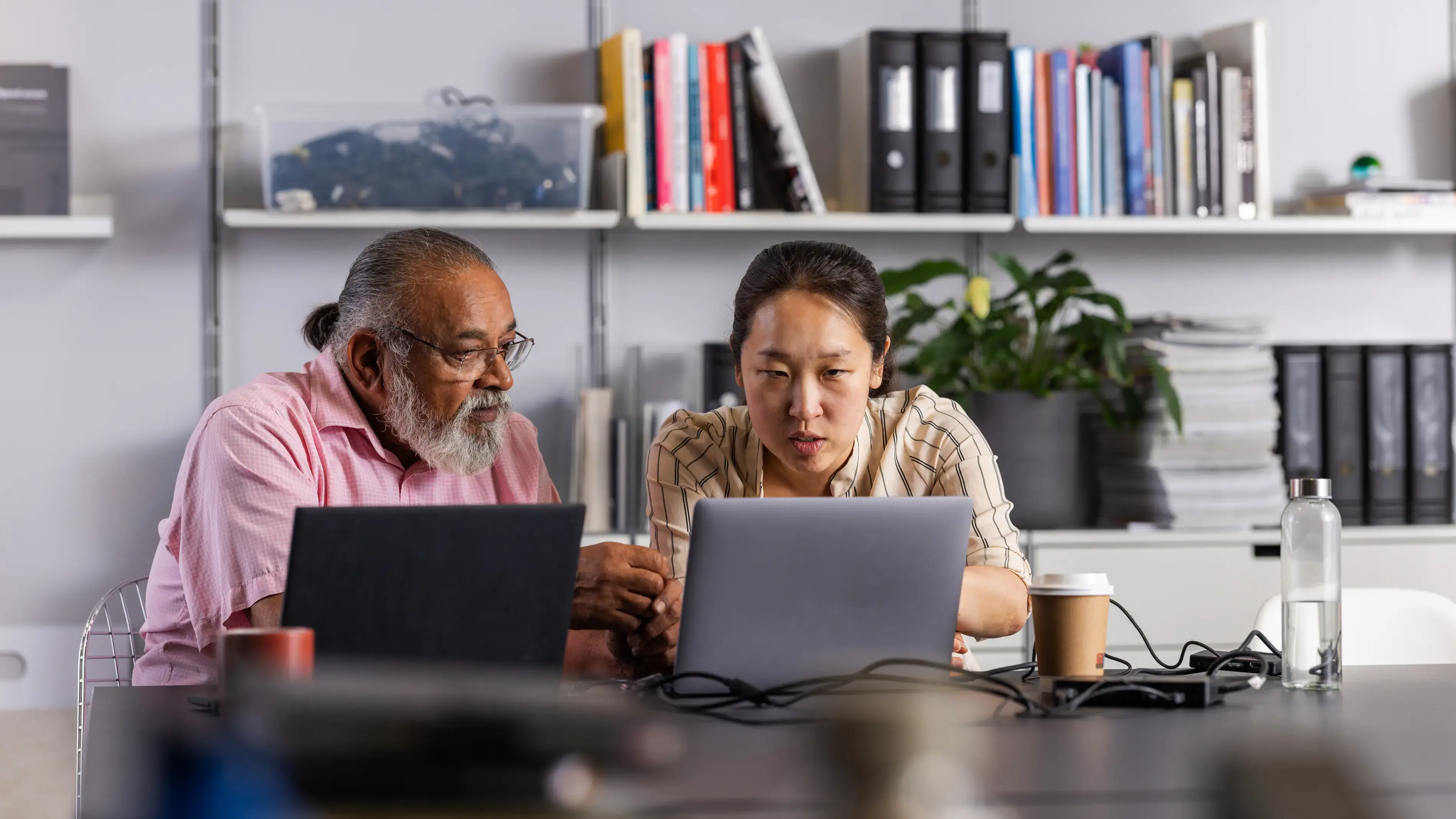 Two coworkers collaborate at laptops.