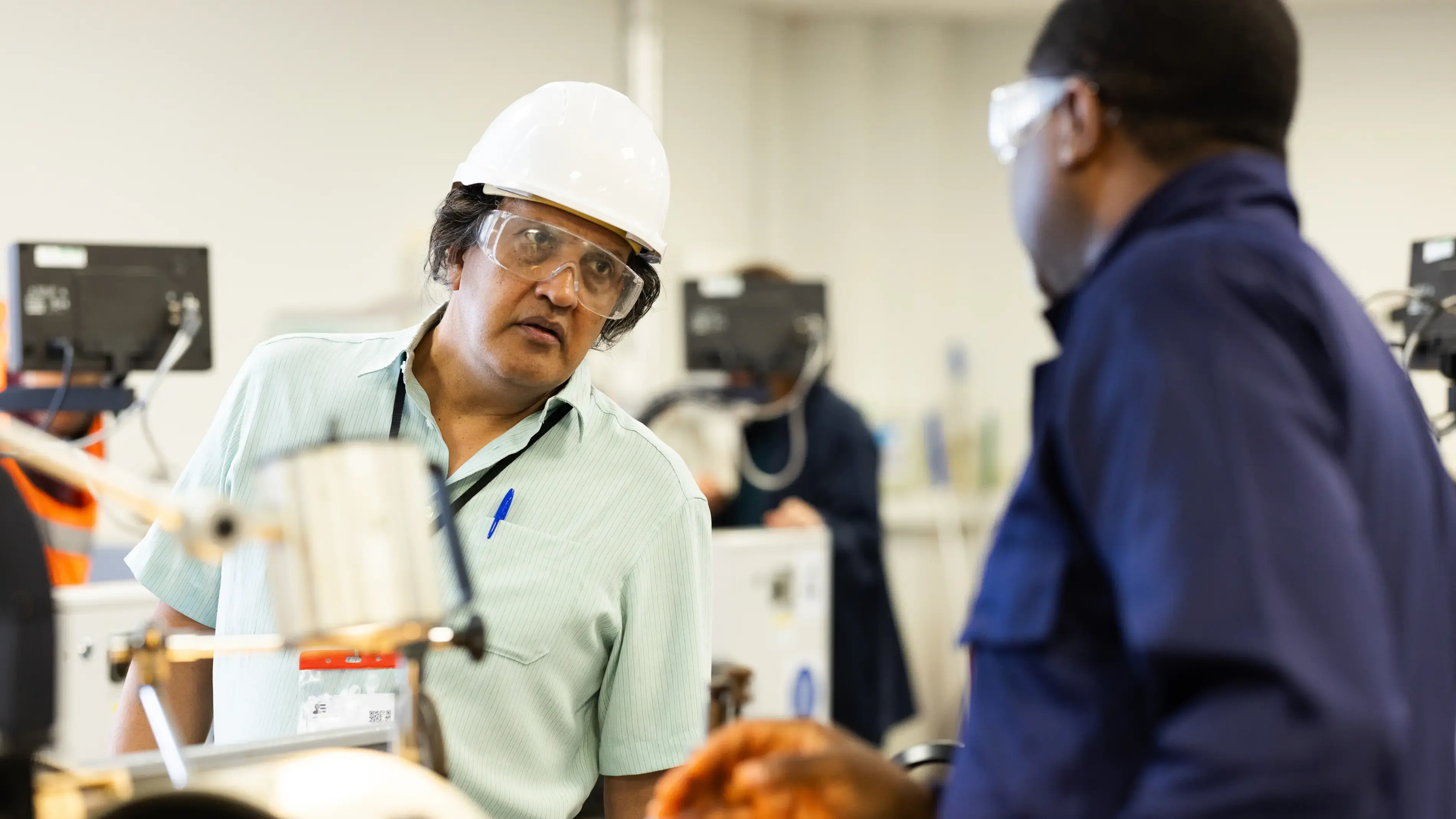 Two coworkers discuss a machine in a workshop.