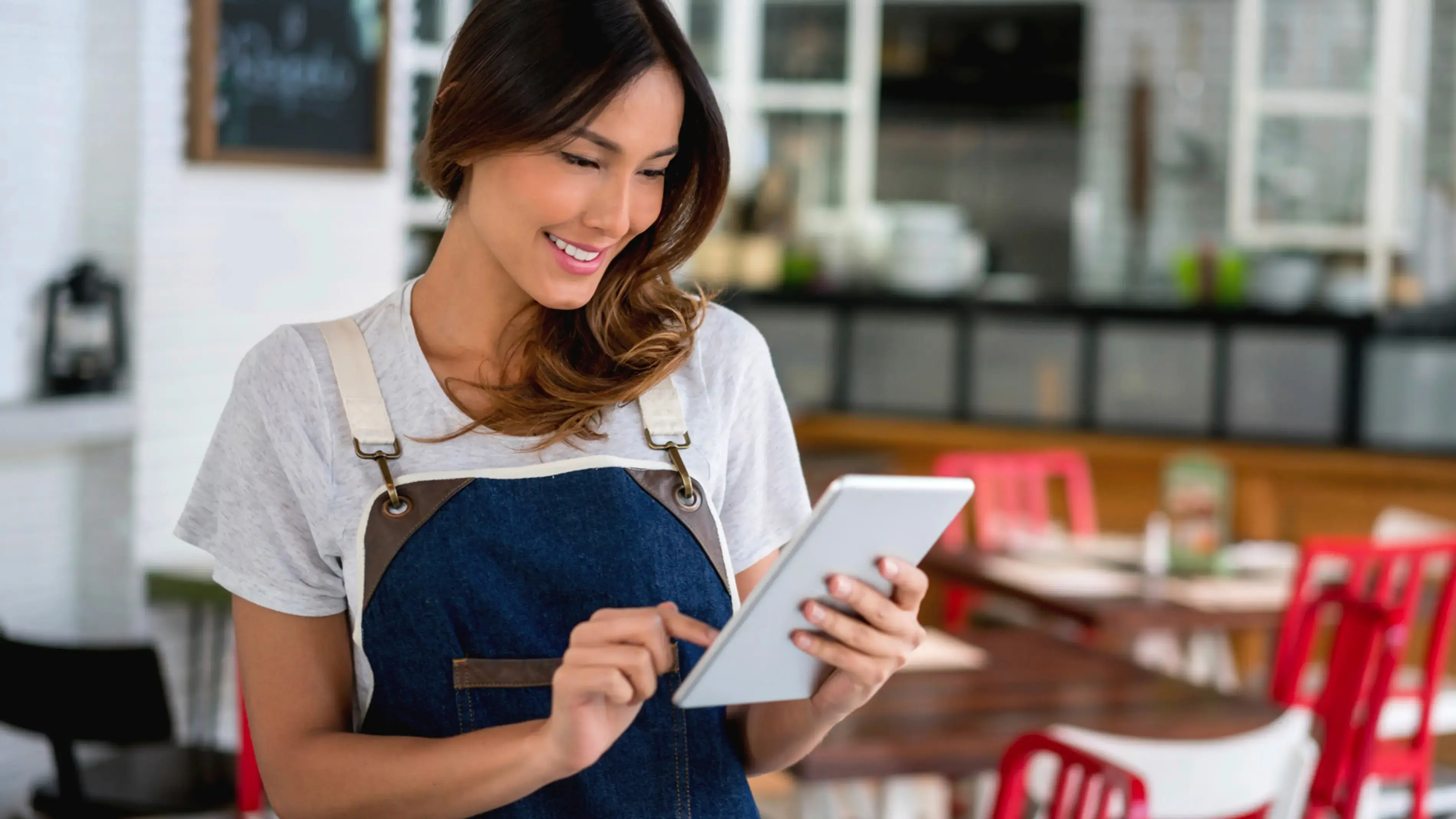 Um empregado sorridente, com um avental azul, usa um tablet com ecrã tátil num restaurante.