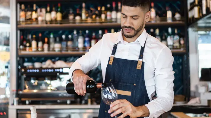 Bartender pouring wine behind a bar.
