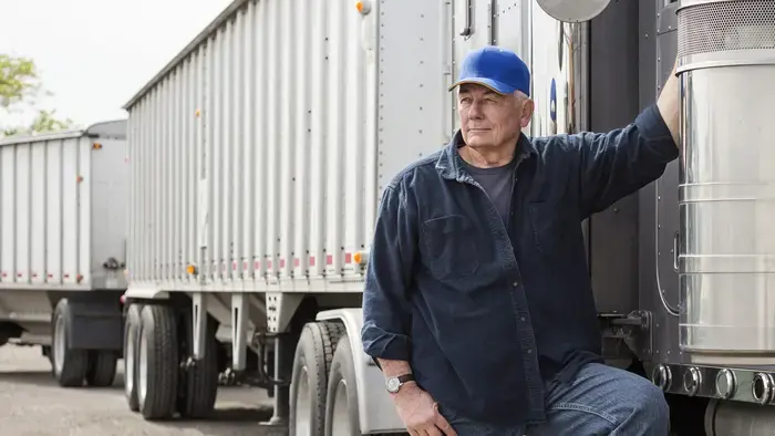 A trucker leans against his semi-truck.
