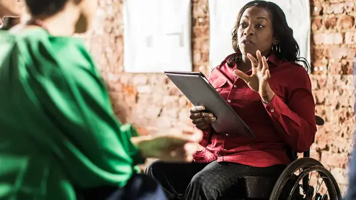 A woman in a wheelchair makes a point, holding a tablet.