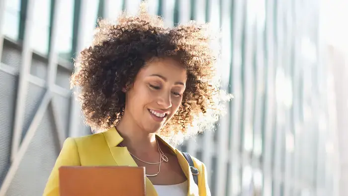 A woman in a yellow jacket smiles while using her smartphone.