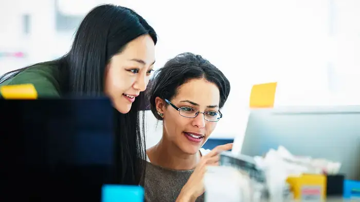 Two coworkers look at a computer screen together, smiling.