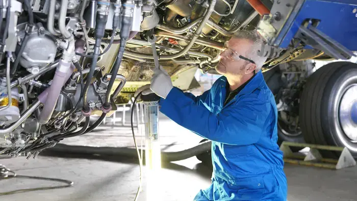 Um mecânico de uniforme azul inspecionando componentes de avião.