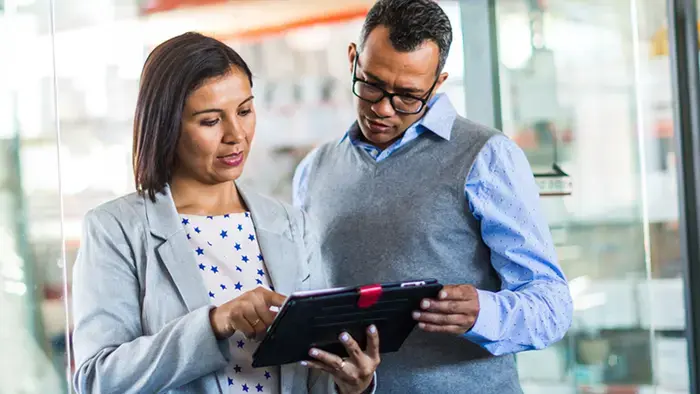 Dois colegas de trabalho olhando juntos para uma tela sensível ao toque.