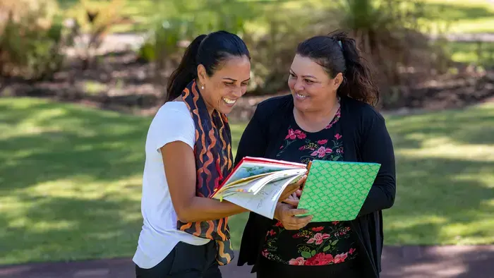 Duas mulheres no campus, rindo de livros, do lado de fora.
