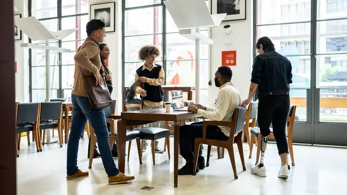 Pessoas se reúnem em torno de uma mesa em um espaço de trabalho, discutindo assuntos relacionados ao trabalho.
