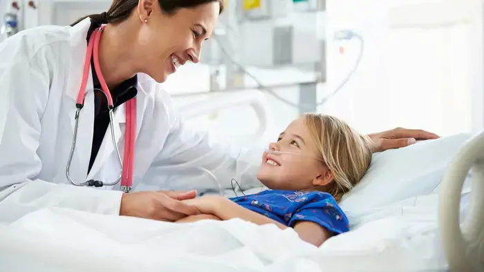 Doctor smiling, leaning over and holding hand of a smiling child patient in a hospital bed
